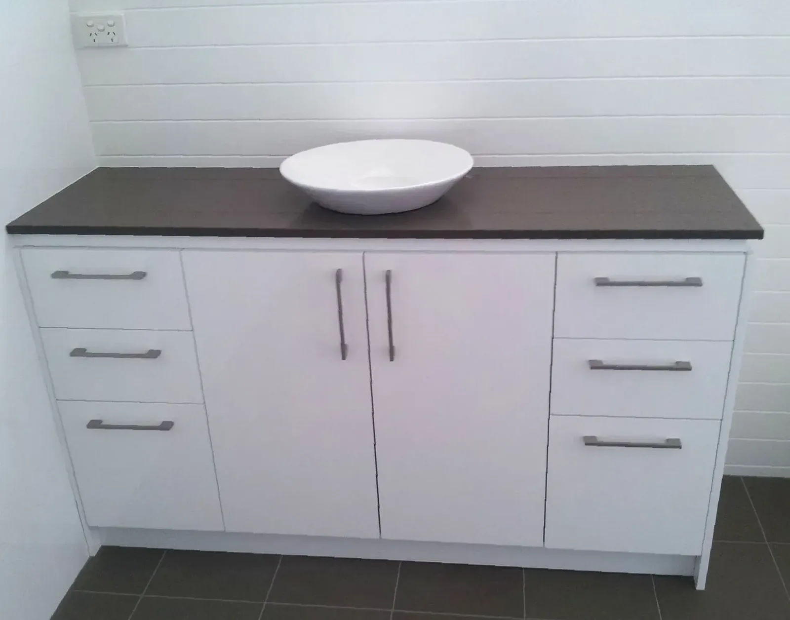 Wide white bathroom vanity with dark benchtop and round vessel basin
