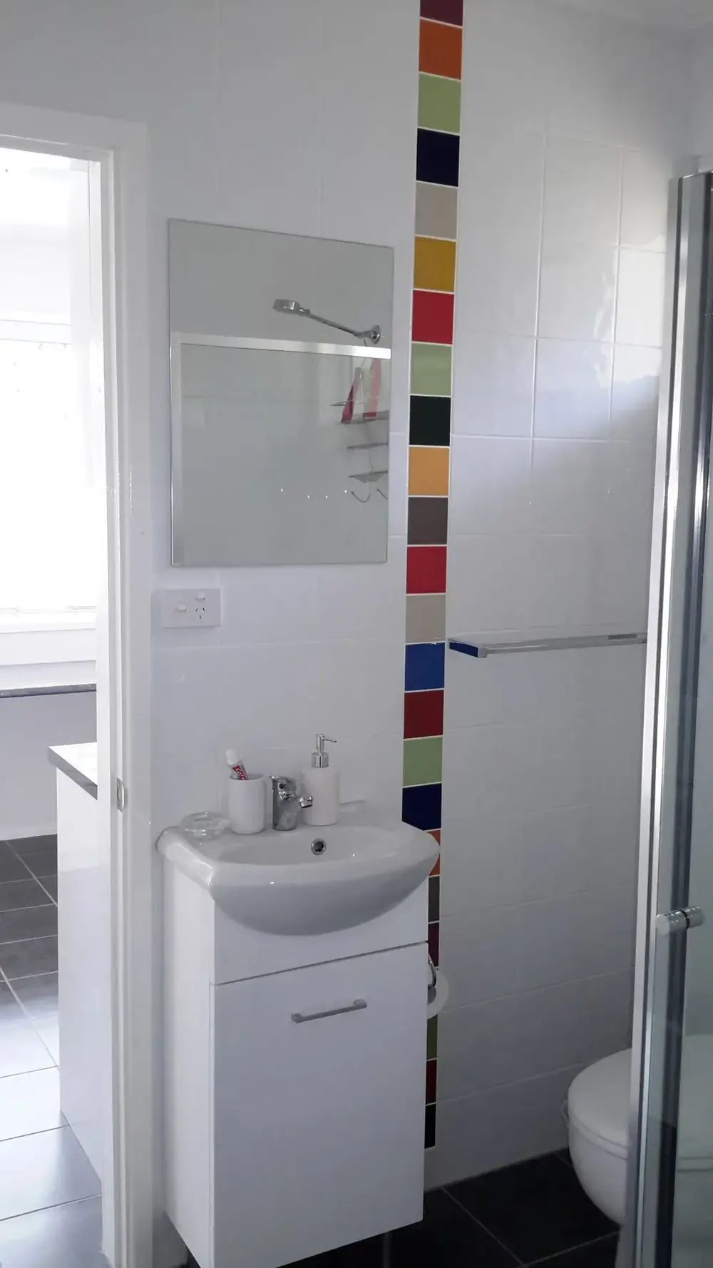 White bathroom vanity with mirror and a vertical strip of colourful tiles