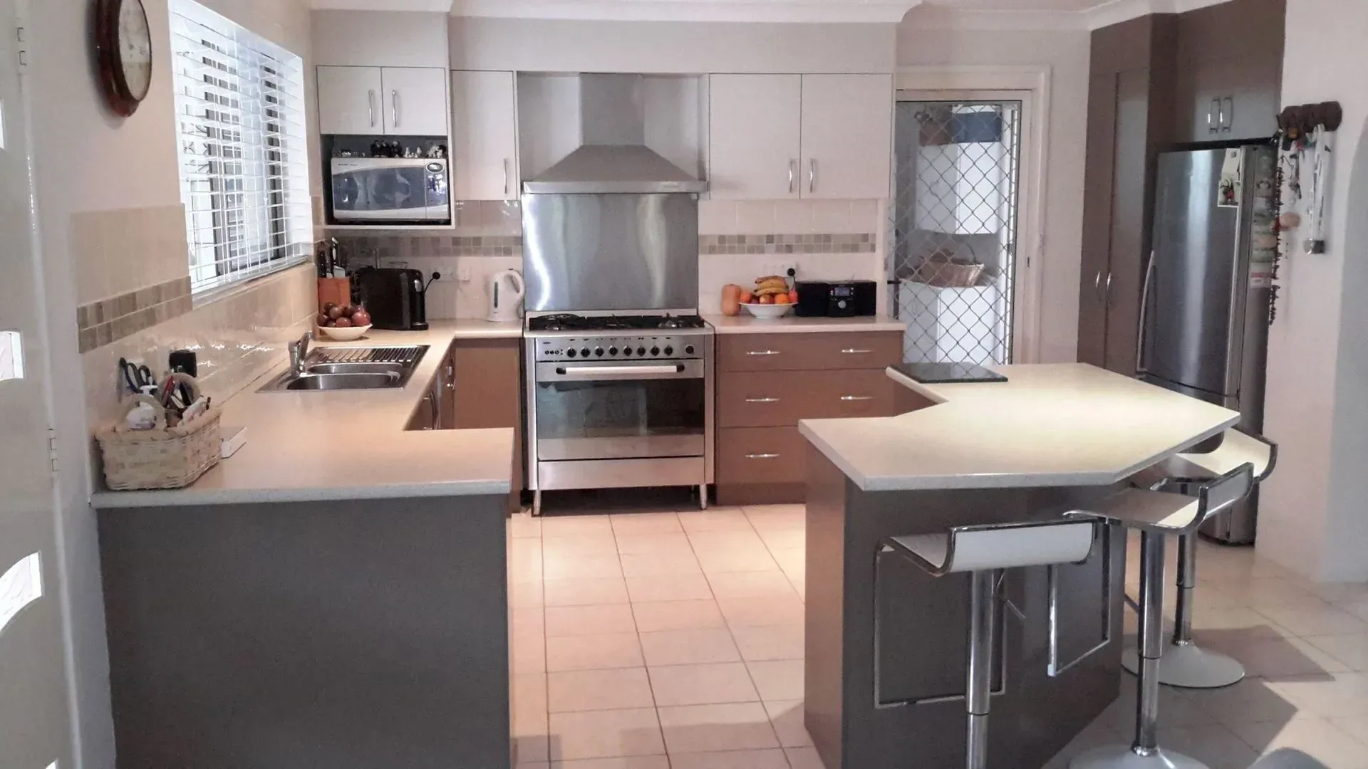 Kitchen with white and taupe cabinetry, island seating and stainless rangehood