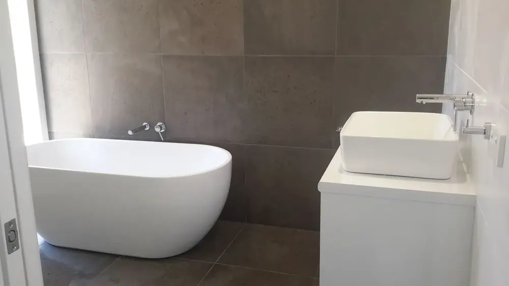 Bathroom with freestanding bath and white vanity against large grey tiles