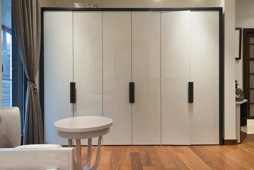 Floor-to-ceiling white wardrobe with black handles beside a small round table