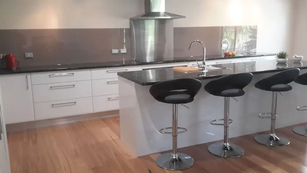 White kitchen with dark benchtop, island seating and stainless rangehood