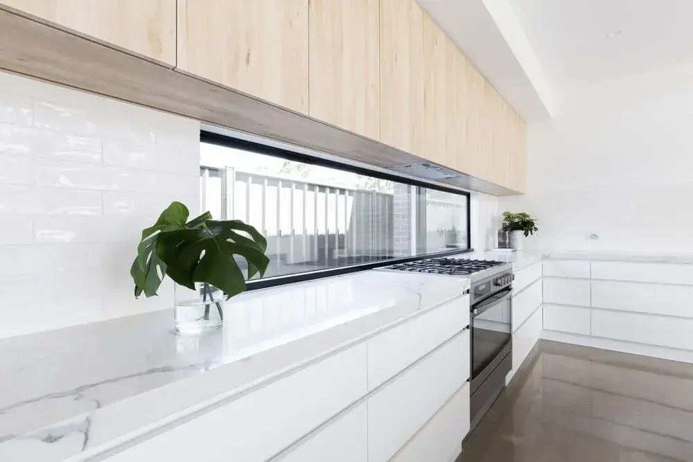 Bright white kitchen with long window, white benchtops and timber overhead cabinetry