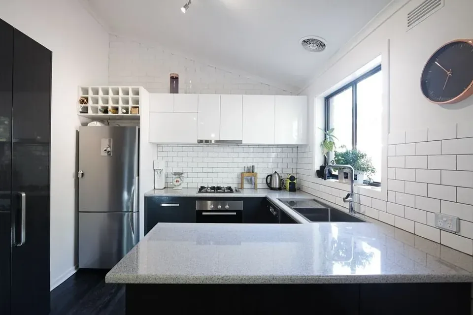 White and black kitchen with stone-look peninsula benchtop and tiled splashback