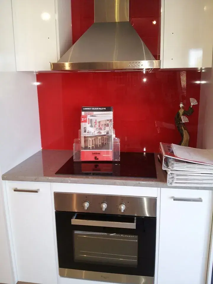 Compact red and white kitchen with benchtop beside a stainless oven and rangehood