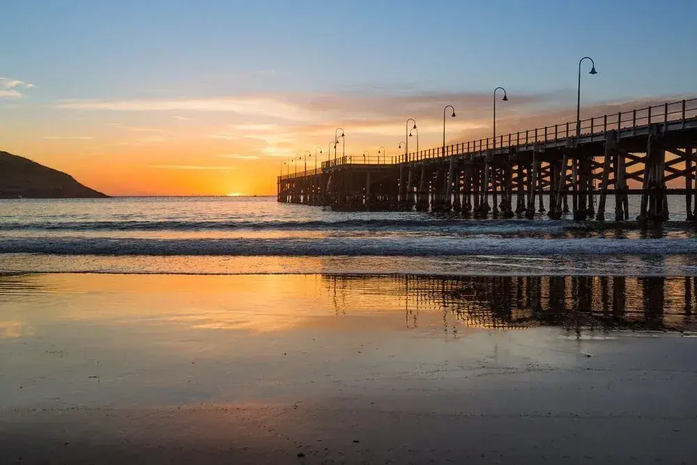 Long timber jetty reflected in wet sand at sunset