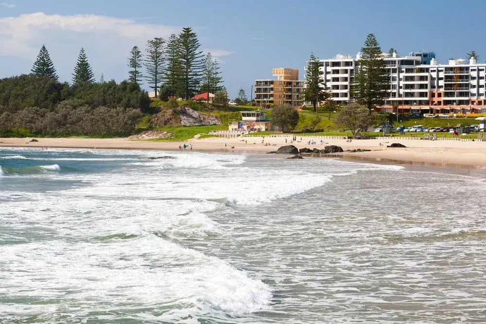 Ocean waves rolling towards a beach with buildings behind the shoreline