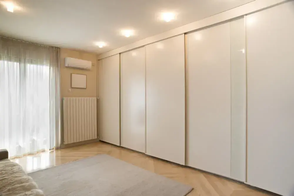Wall of tall white built-in wardrobe doors in a light bedroom
