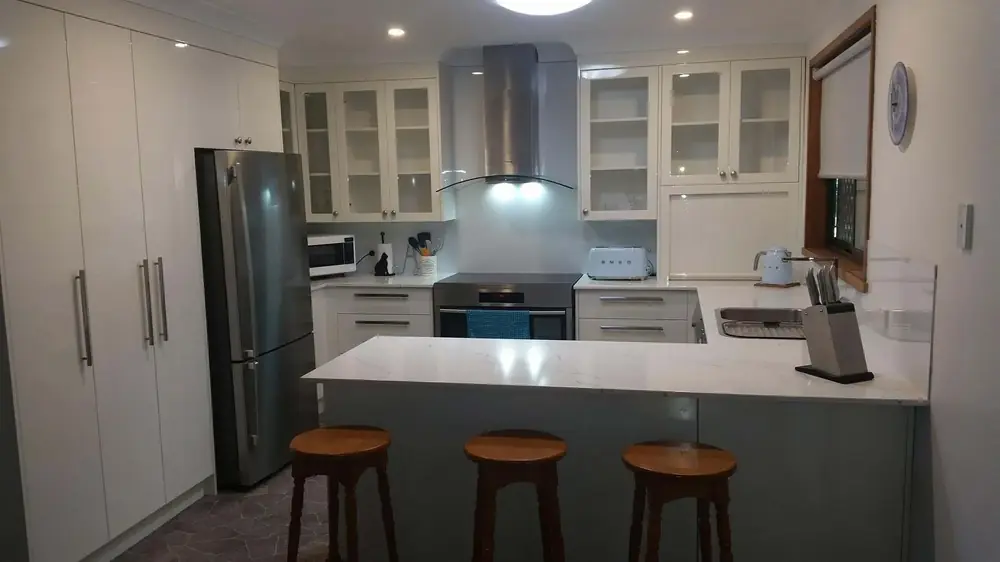 Kitchen with white island benchtop, glazed cabinets and stainless appliances